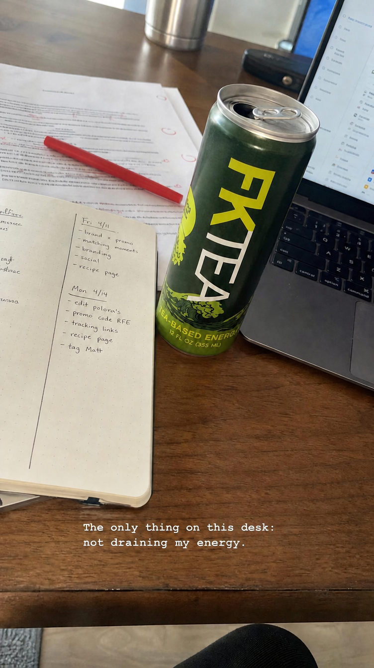 An FKTea can beside a laptop, notebook, and marked-up work.