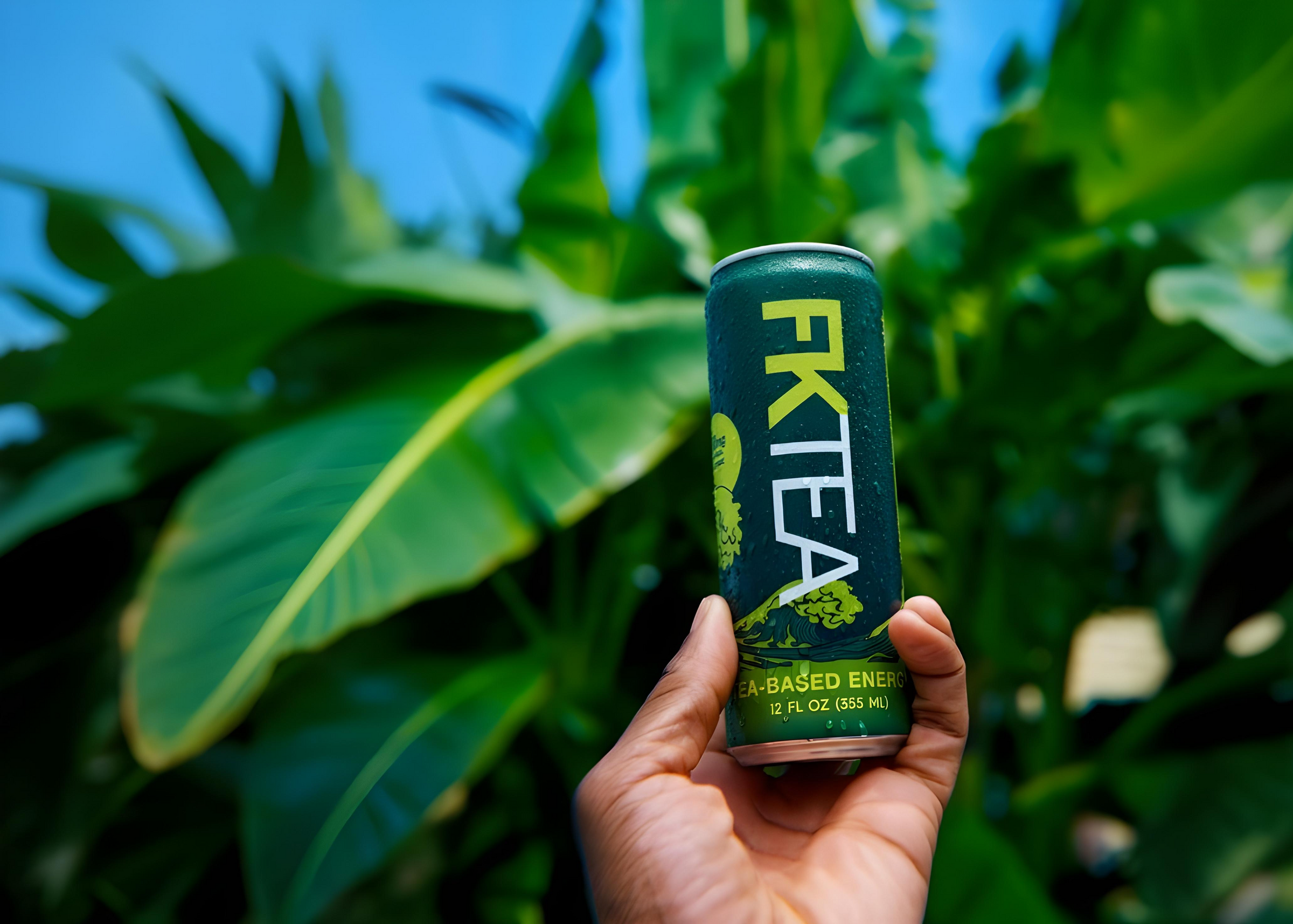 Hand holding a can of FKTea against a green leafy background